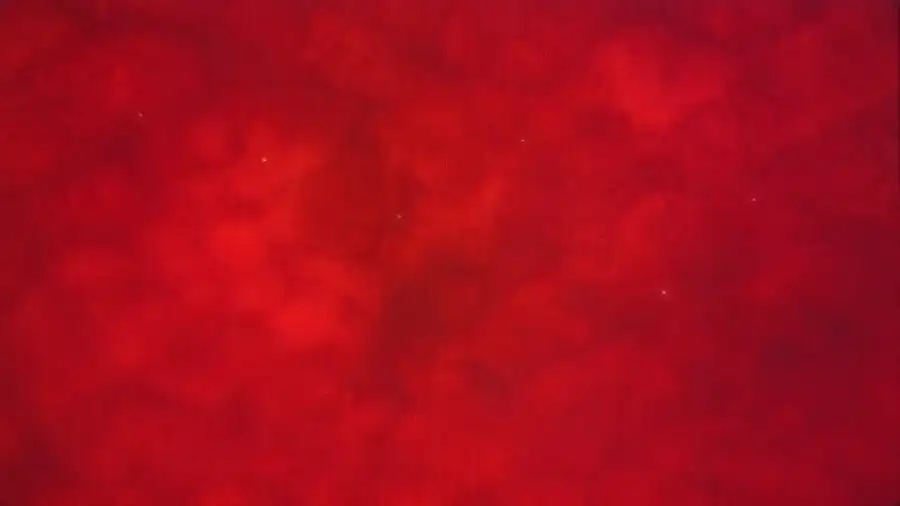 Microscope view with a cluster of faint glowing dots on a deep red background